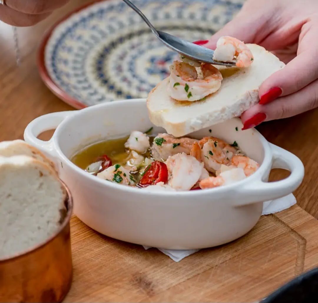 Gambas al ajillo em tigela branca com alho e pimenta, servidas sobre pão