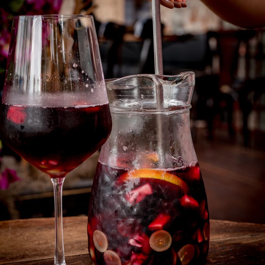 Jarra de sangria tinta com frutas e taça servida sobre mesa de madeira